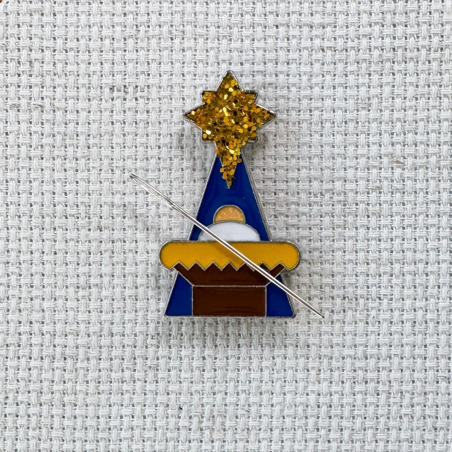 Magnetic enamel needle minder featuring a festive Christmas Nativity Manger scene, designed to hold needles securely while stitching.