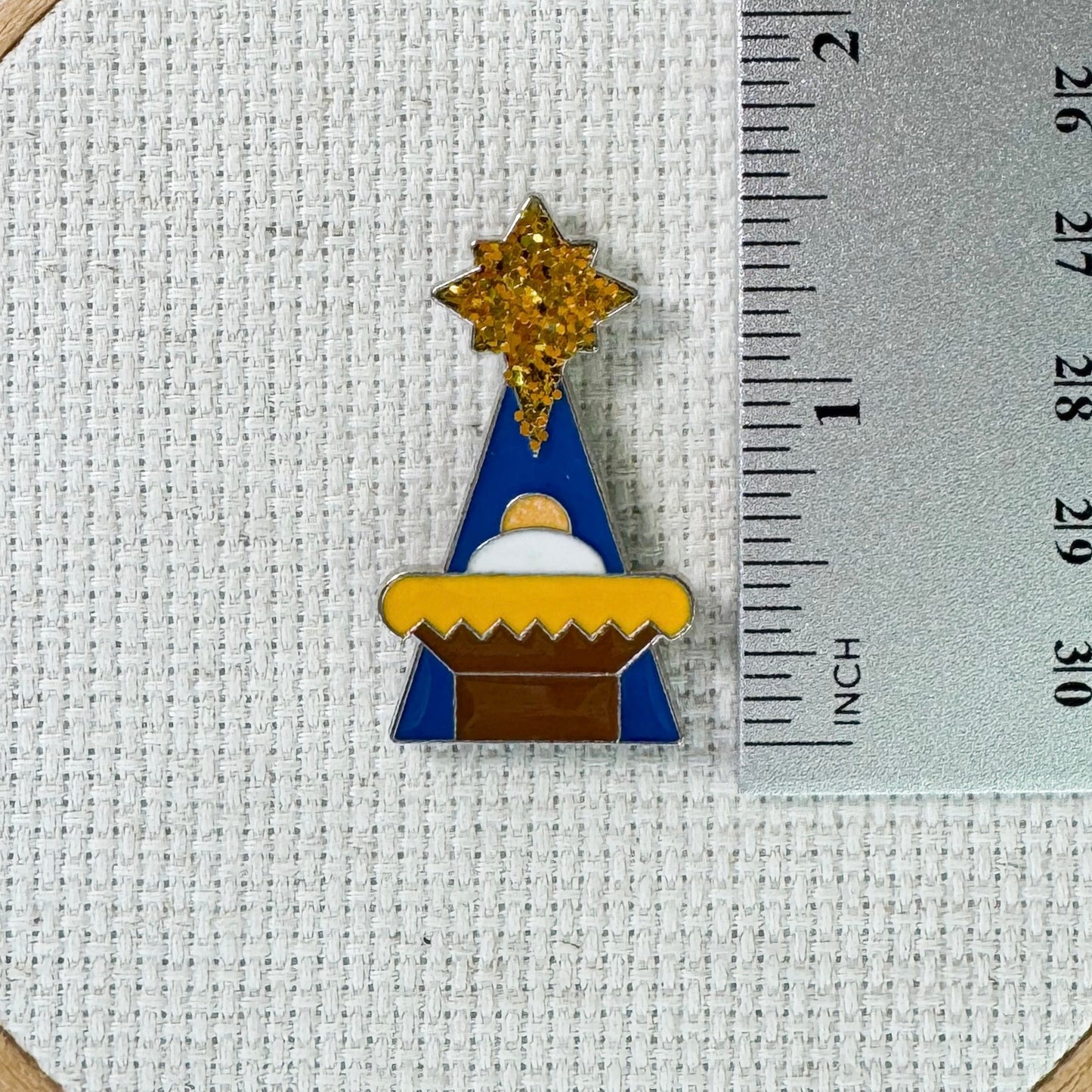Magnetic enamel needle minder featuring a festive Christmas Manger scene, designed to hold needles securely while stitching.