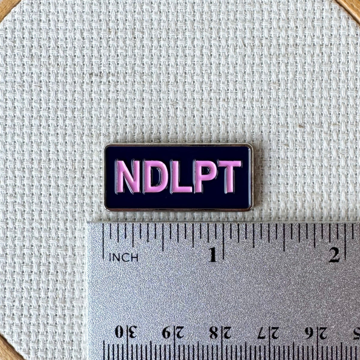 NDLPT magnetic enamel needle minder shown with ruler for size measurement, approximately 1.25 inch needle minder.