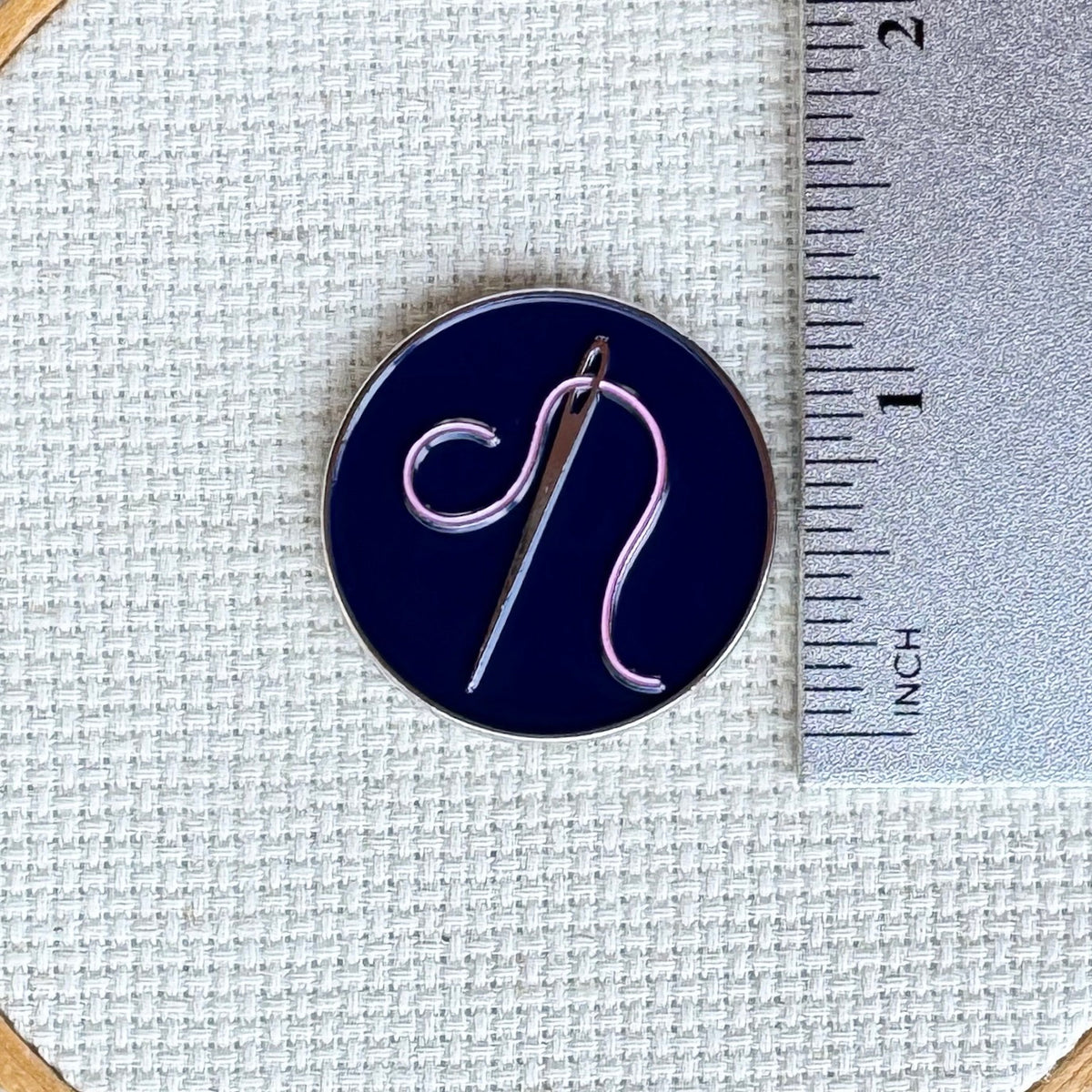 Needle and pink thread needle minder shown with ruler for size measurement, approximately 1.25 inch needle minder.