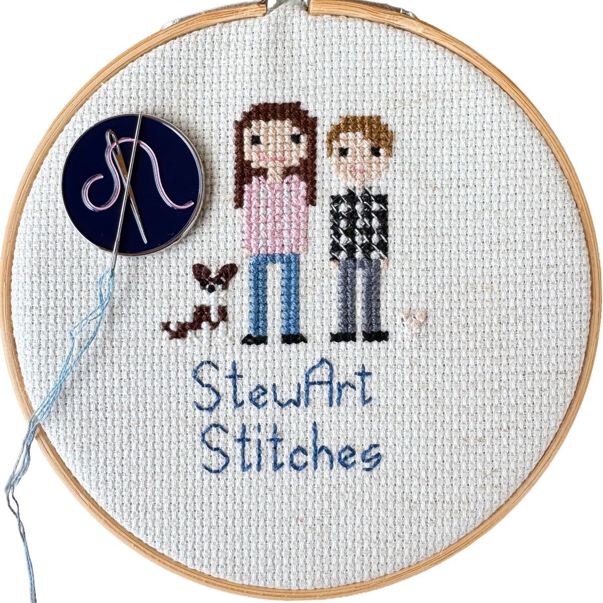 Needle and pink thread needle minder holding a needle on a  cross stitch canvas while stitching.