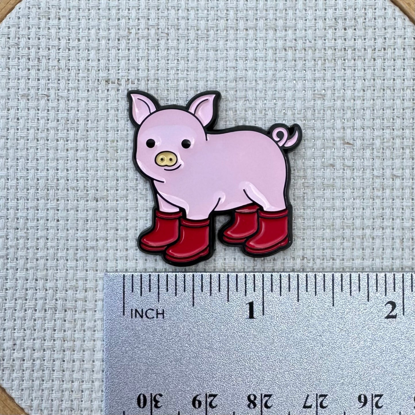 Pig with Red Boots Enamel Needle Minder needle minder shown with ruler for size measurement, approximately 1.25 inch.
