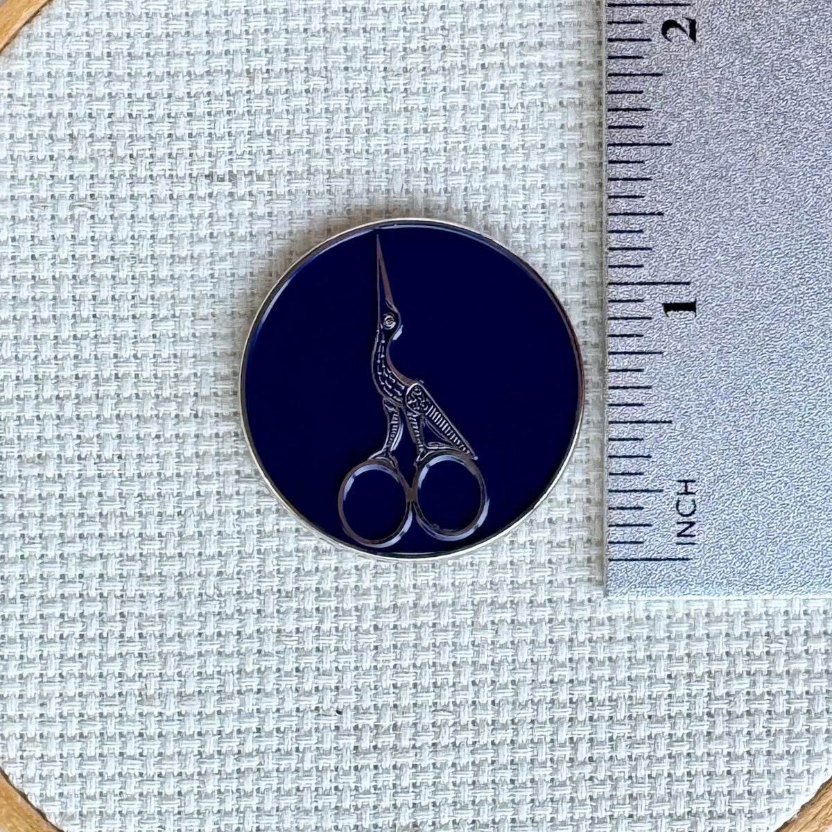 Stork scissors needle minder shown with ruler for size measurement, approximately 1.25 inch needle minder.