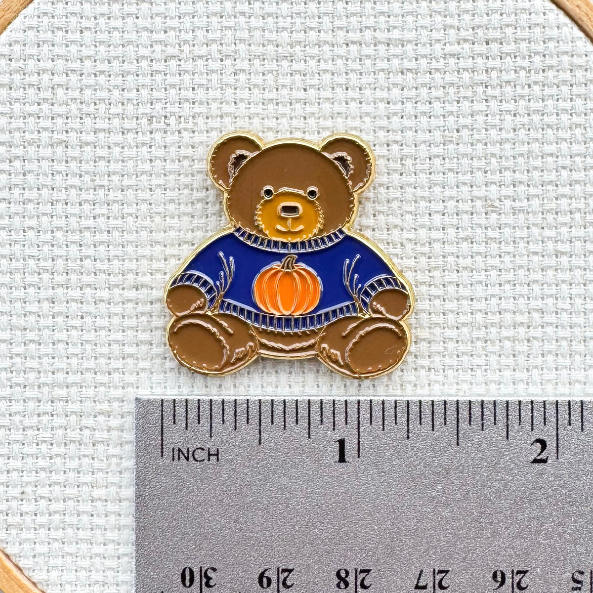 Teddy bear enamel needle minder wearing a blue sweater with a pumpkin, magnetic needle holder for cross stitch, needlepoint, embroidery, quilting, sewing and other stitching projects.