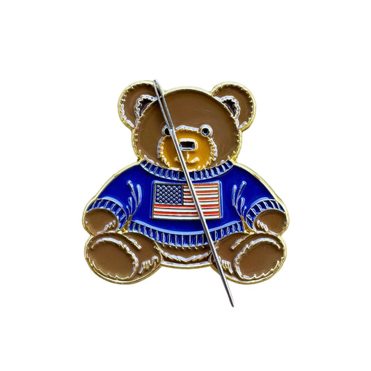 Teddy bear enamel needle minder wearing a blue sweater with an American flag, magnetic needle holder for cross stitch, needlepoint, embroidery, quilting, sewing and other stitching projects.