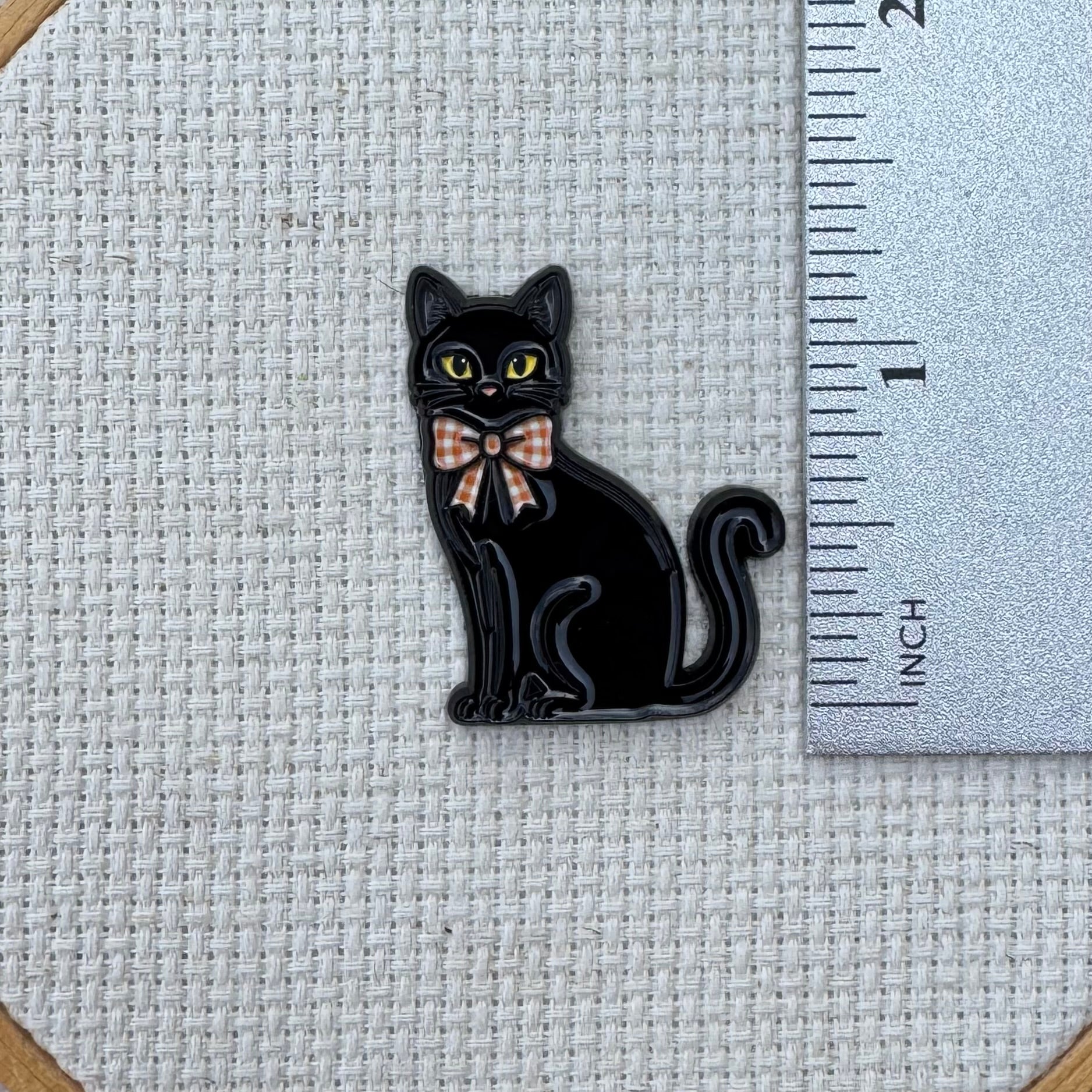Black cat needle minder shown with ruler for size measurement, approximately 1.25 inch.
