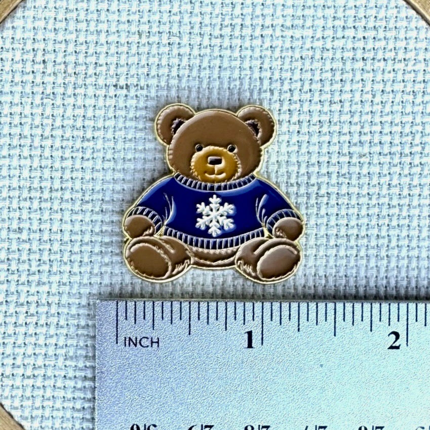 Teddy bear enamel needle minder wearing a blue sweater with a snowflake, magnetic needle holder for cross stitch, needlepoint, embroidery, quilting, sewing and other stitching projects.